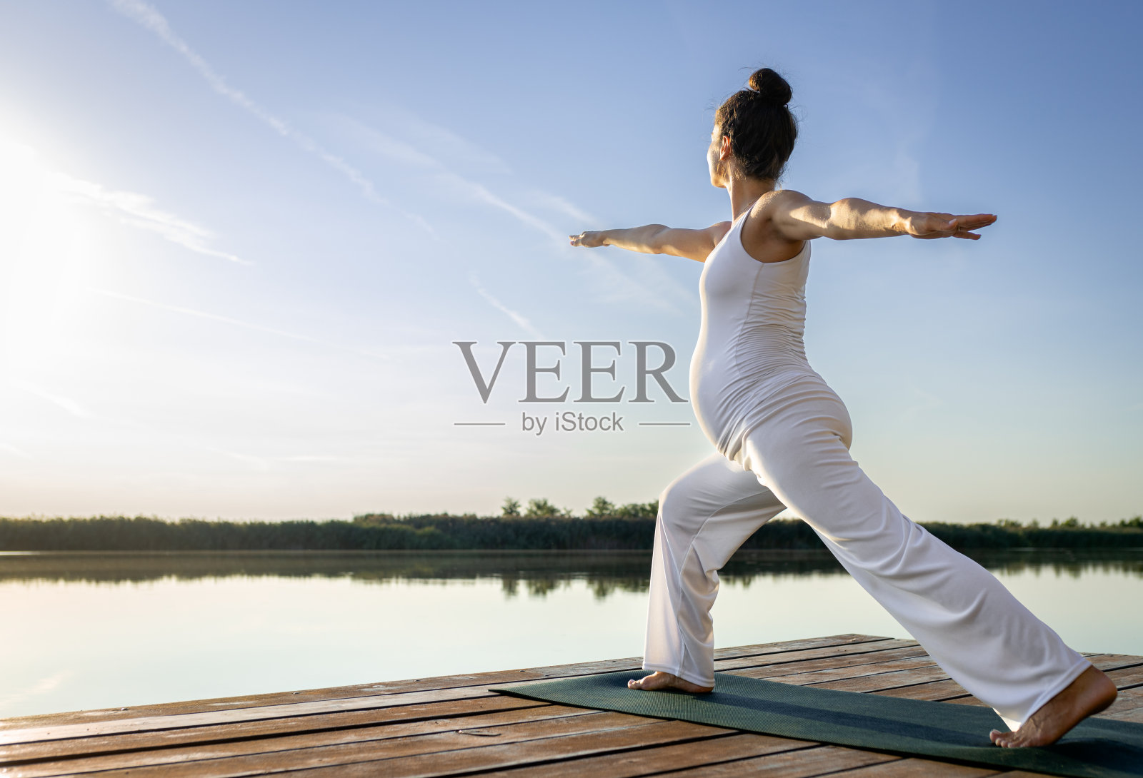 一名孕妇白天在湖边做瑜伽。照片摄影图片