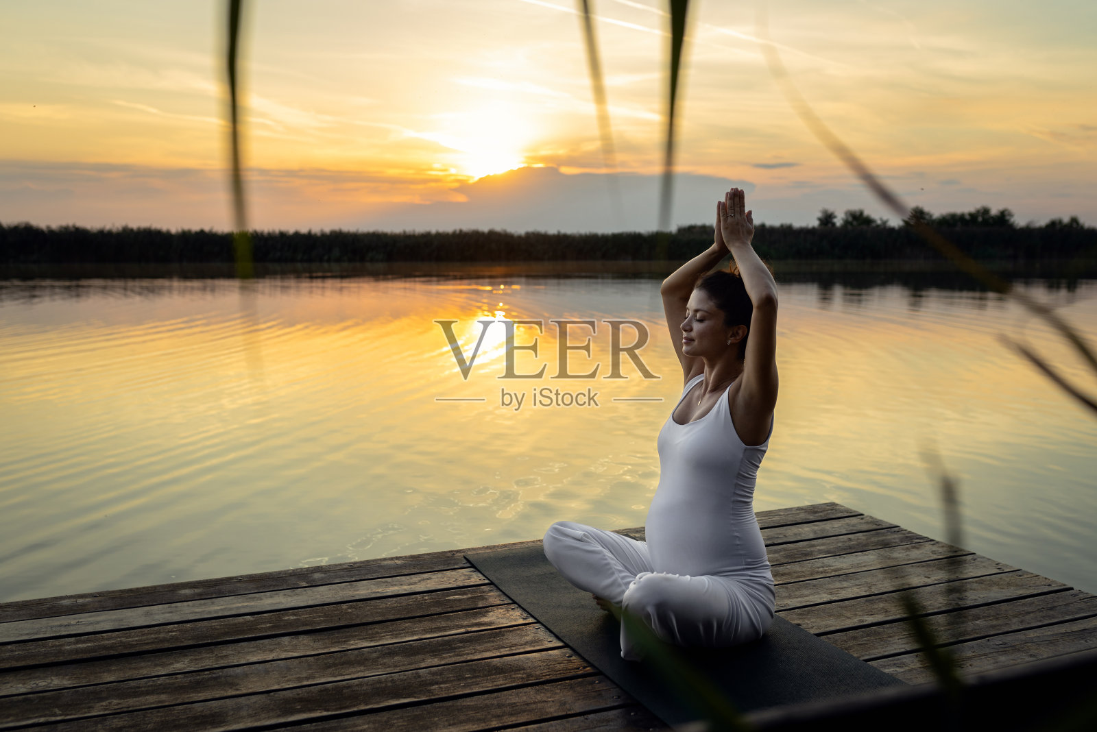 日落时分，孕妇在湖边做瑜伽。照片摄影图片