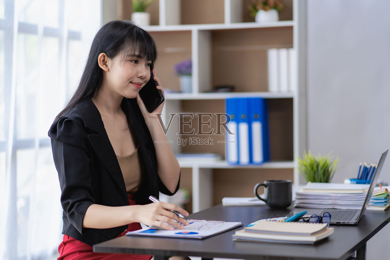 亚洲女商人使用笔记本电脑和移动智能手机与同事和客户沟通。运用现代科技在财务概念办公室执行和协调工作。照片摄影图片