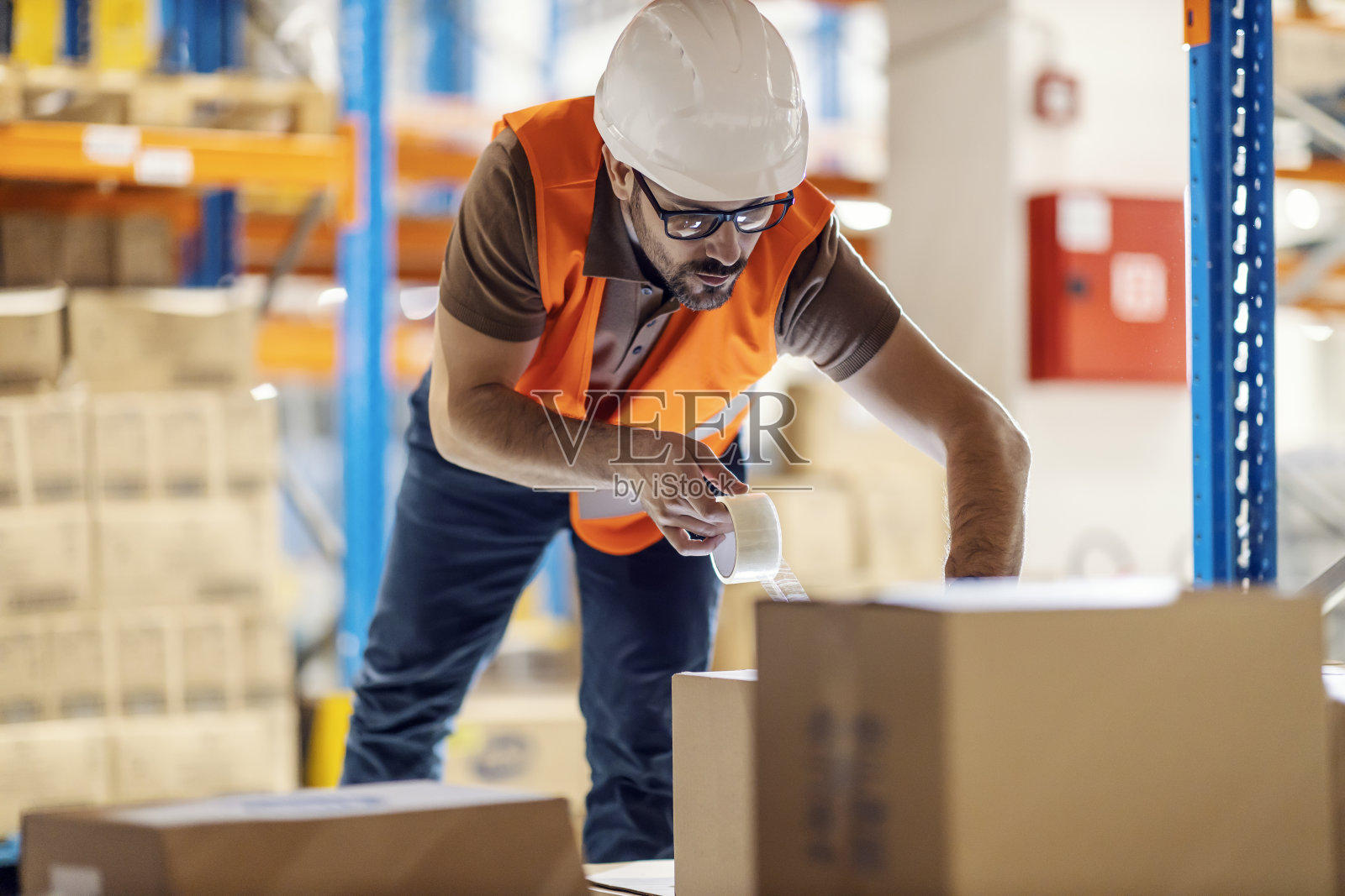 一名仓库工人用管道胶带把货物封在箱子里。照片摄影图片