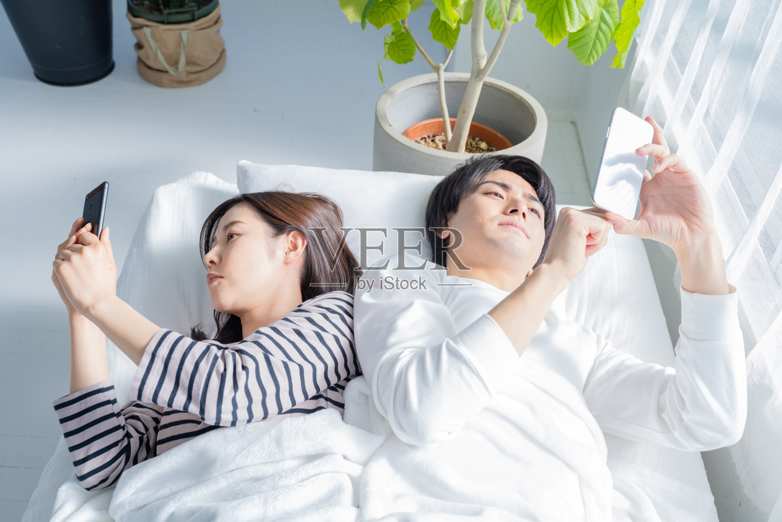 情侣在床上看智能手机。照片摄影图片