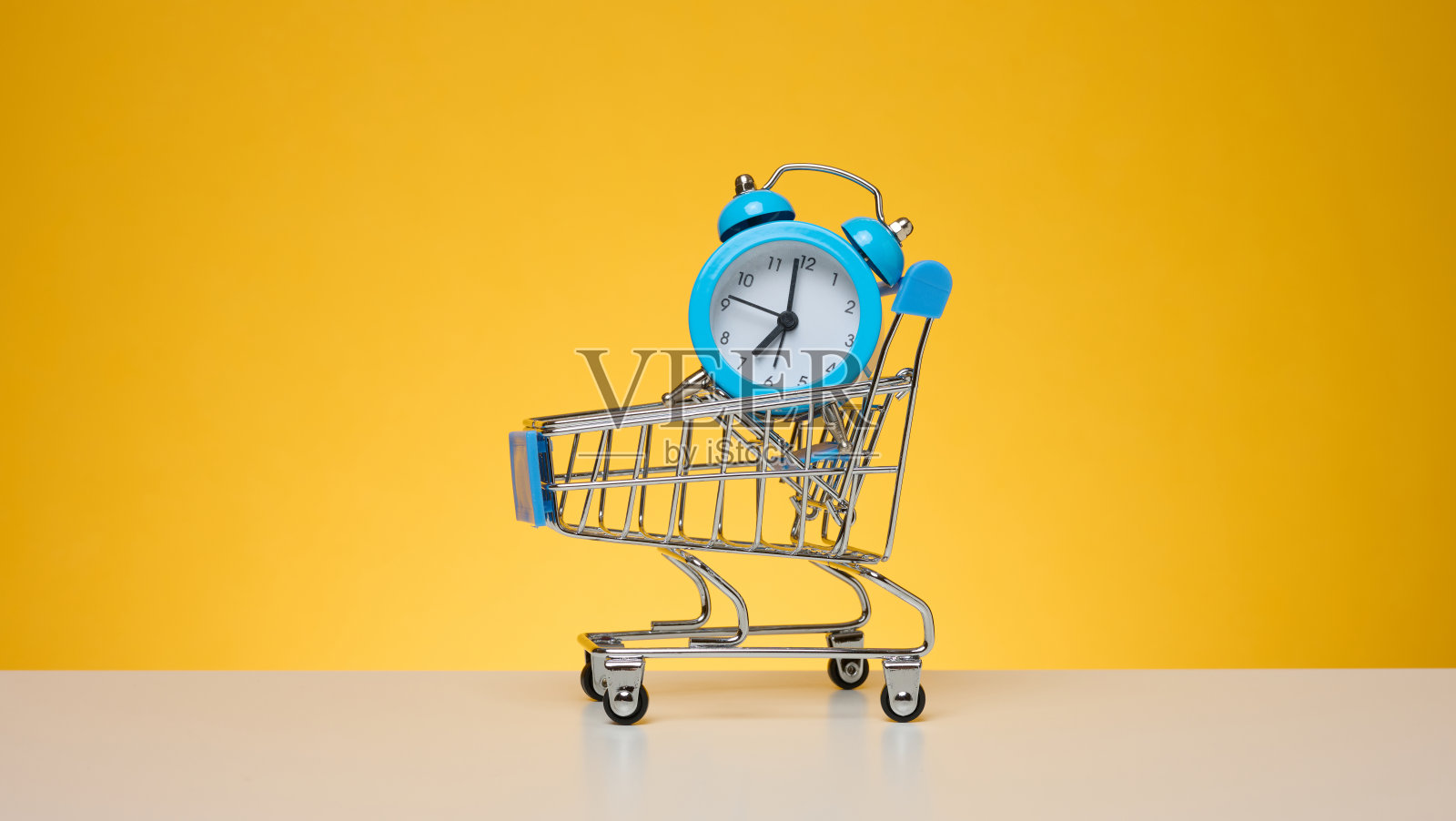 黄色背景的迷你购物车里的圆形闹钟照片摄影图片