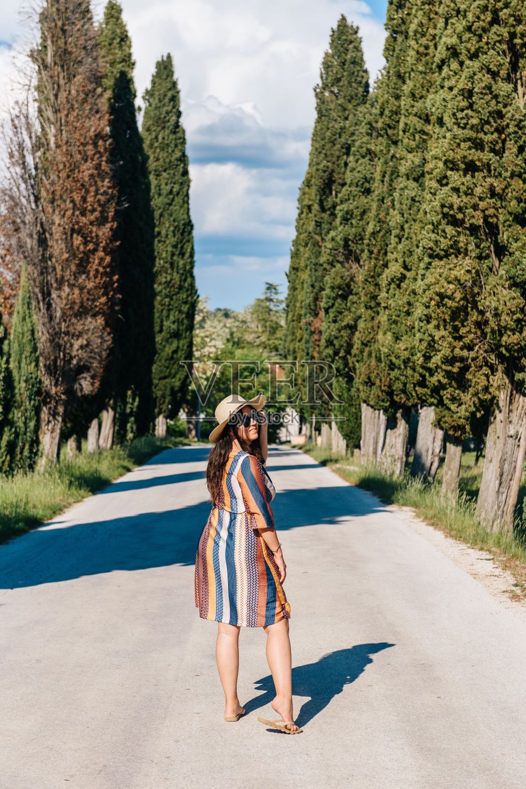 在托斯卡纳，穿着裙子的美丽女子站在绿树环绕的道路上回头看照片摄影图片