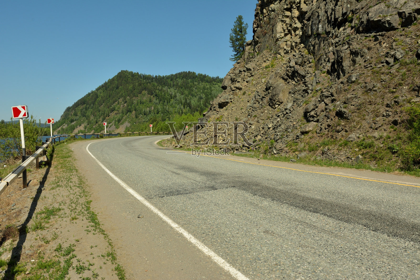 在一个阳光明媚的夏日，在高山脚下一条有栅栏的柏油路右转。照片摄影图片