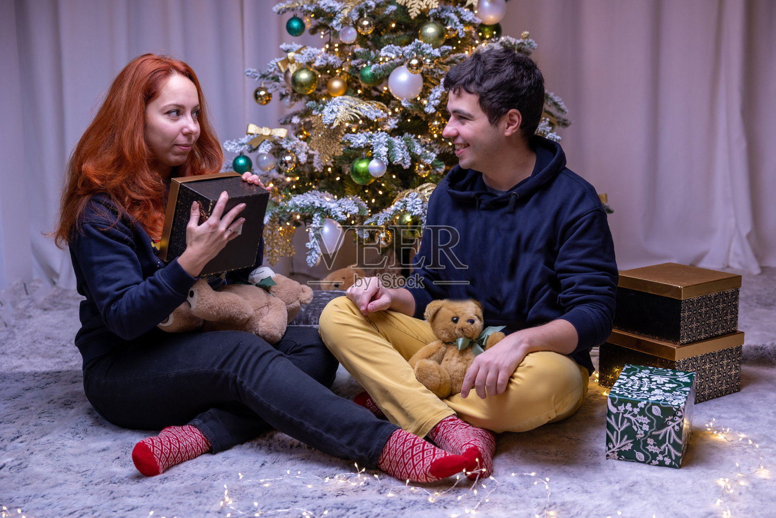 红头发的女孩收到了一个男人送的礼物。背景装饰圣诞树。赠送礼物。照片摄影图片