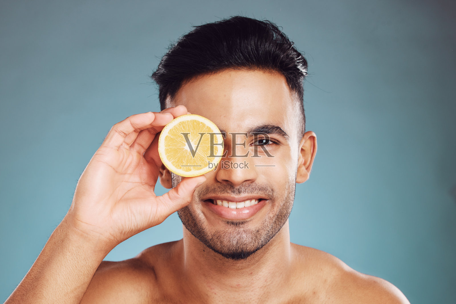 快乐的工作室肖像，男人柠檬护肤美容健康和面部健康的蓝色背景。年轻的快乐模型，美容水果健康的面部皮肤或维生素c与墙背景照片摄影图片