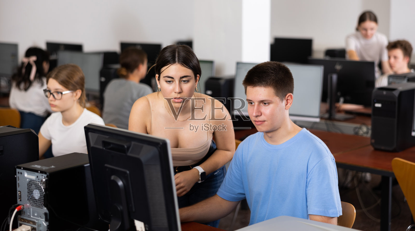 聪明的女少年在电脑教室里给正在使用电脑的男同学提示照片摄影图片