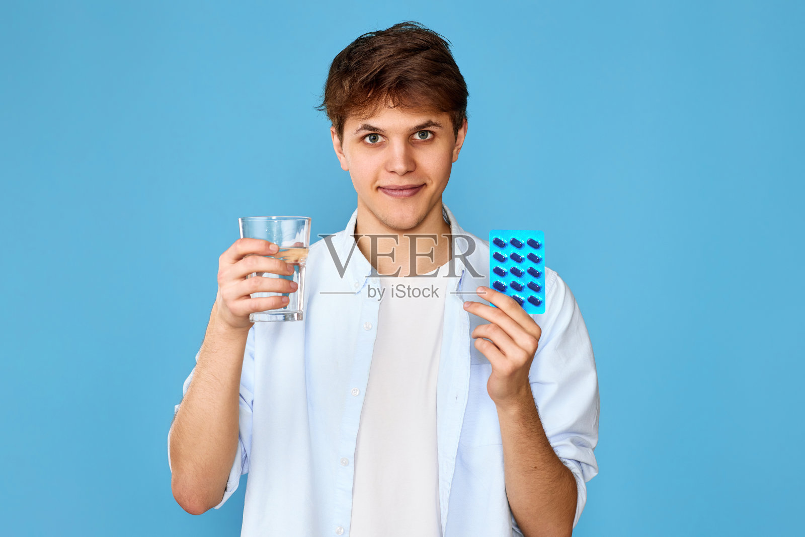 男子拿着药丸和一杯水在蓝色背景照片摄影图片