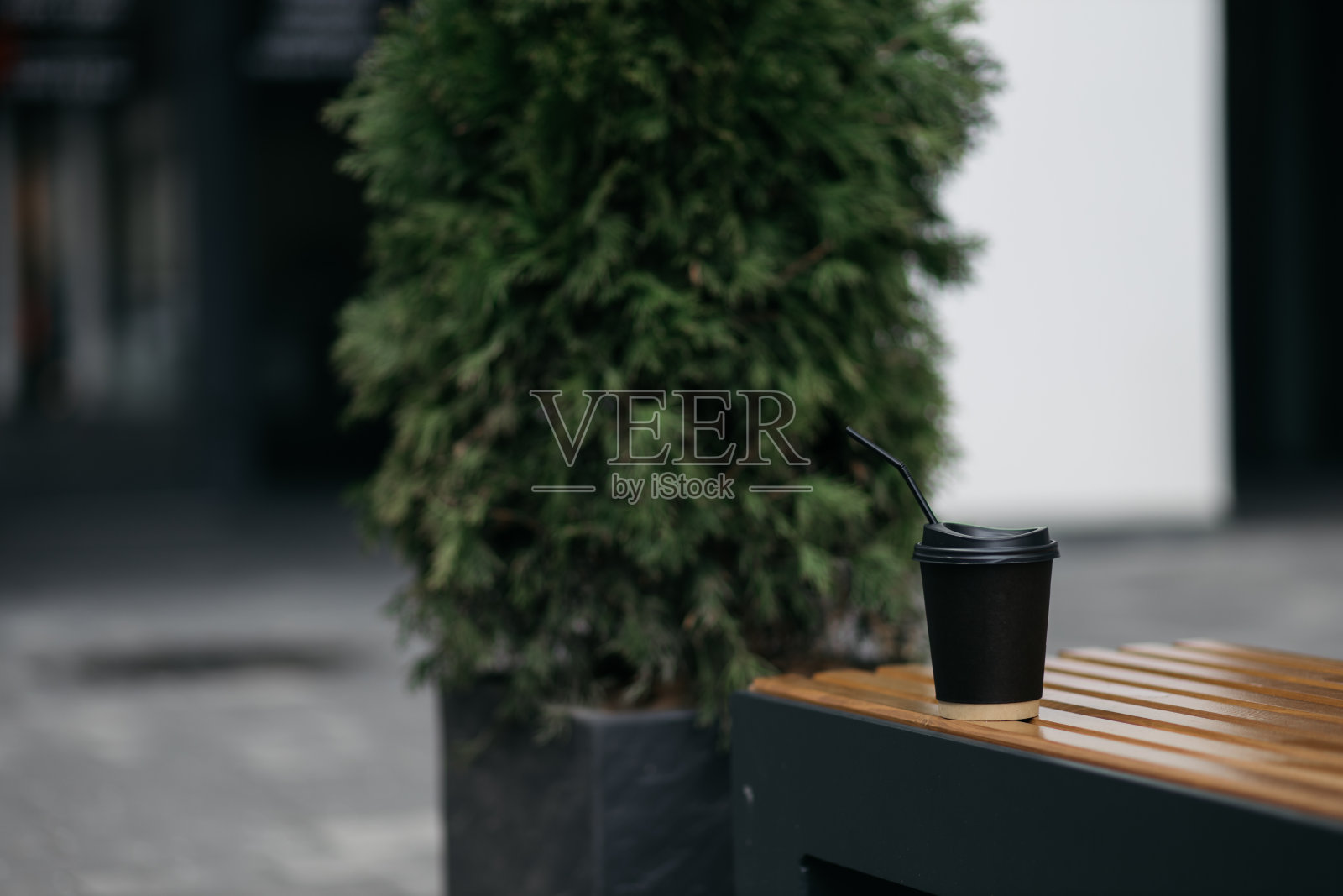 公园的长椅上放着一杯带盖的黑纸杯咖啡。夏日，阳光和耀斑从太阳。暖色调的色彩。照片摄影图片