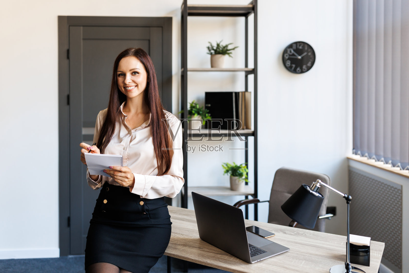快乐的商务女性用笔在笔记本上写着什么，举起手来，做出问候的手势。照片摄影图片