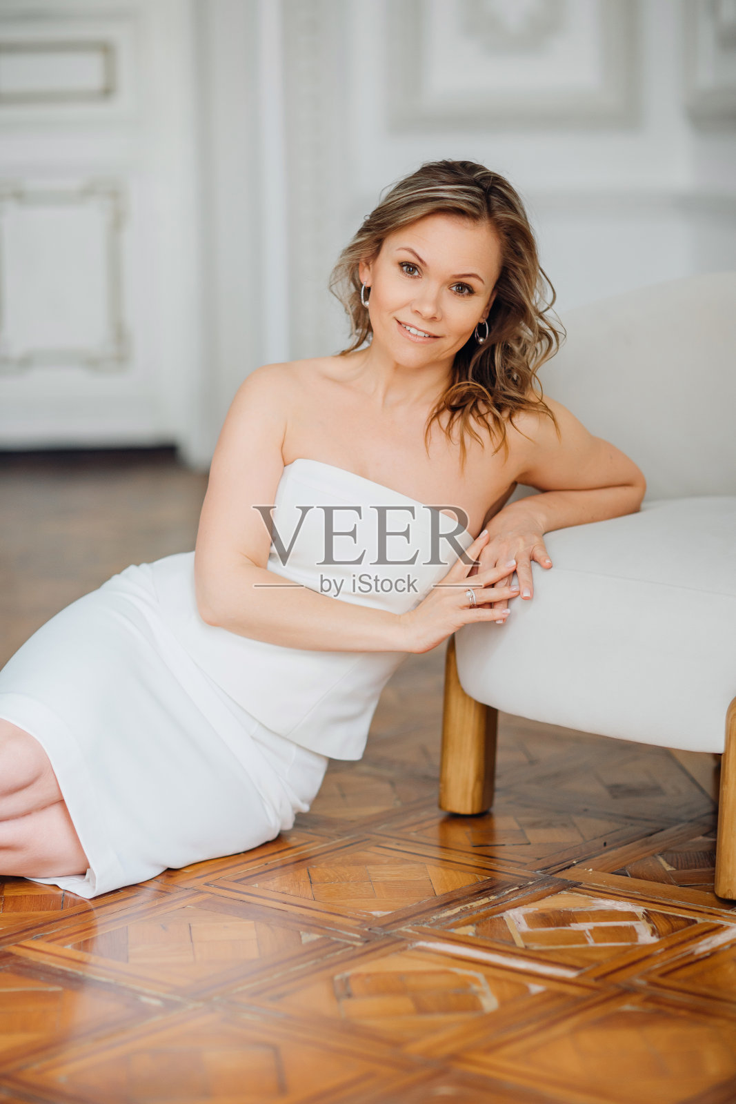 一个穿着白色连衣裙的精致中年妇女坐在椅子旁的地板上照片摄影图片