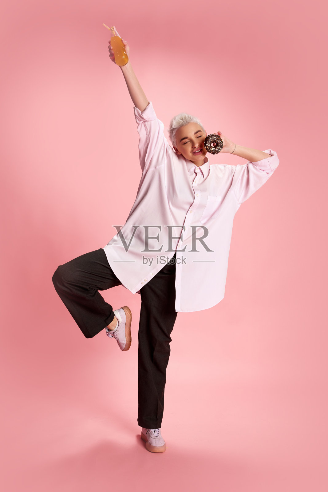 年轻的时尚女性短发的肖像与甜甜圈和橙汁孤立在粉红色的背景。快乐照片摄影图片