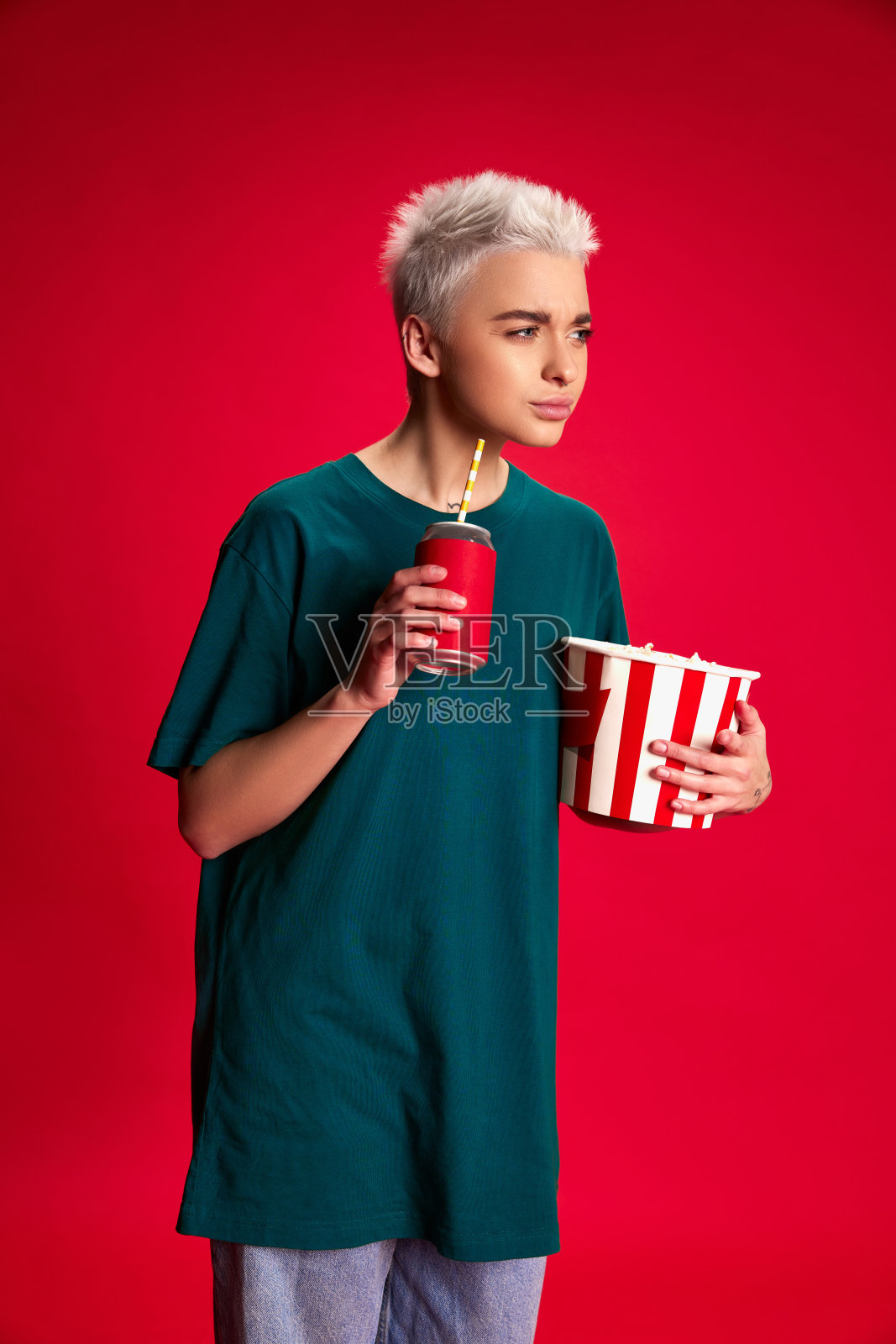 年轻的时尚女性短发的肖像与爆米花篮子孤立在红色背景。看电影照片摄影图片