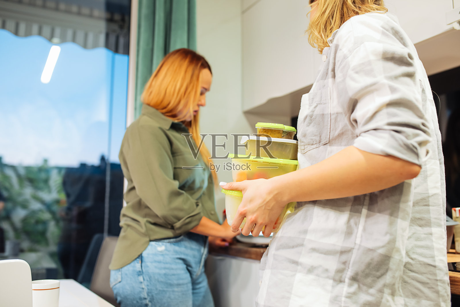 从下面看，两位成年妇女正在为晚餐准备食材。朋友做饭。塑料容器食品。照片摄影图片