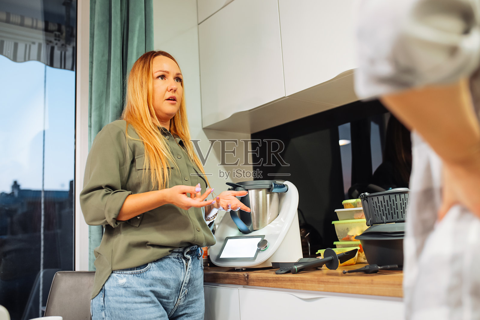 女人们聊天，用现代电子厨房电器做晚餐，侧视图。朋友们一起在家里的厨房做饭。照片摄影图片