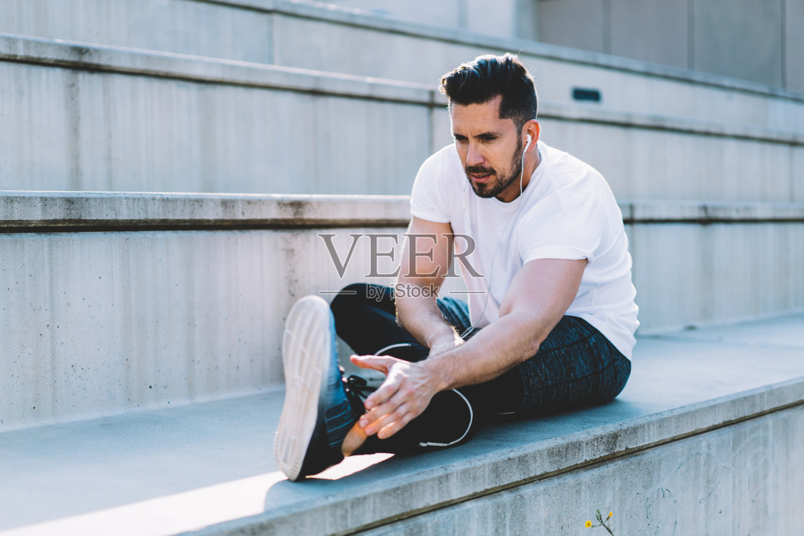 年轻的20多岁男性跑步者在体育场内做有氧运动，戴着耳机听音乐，严肃的运动员穿着运动服在晨练中瘦身，采用运动的生活方式照片摄影图片