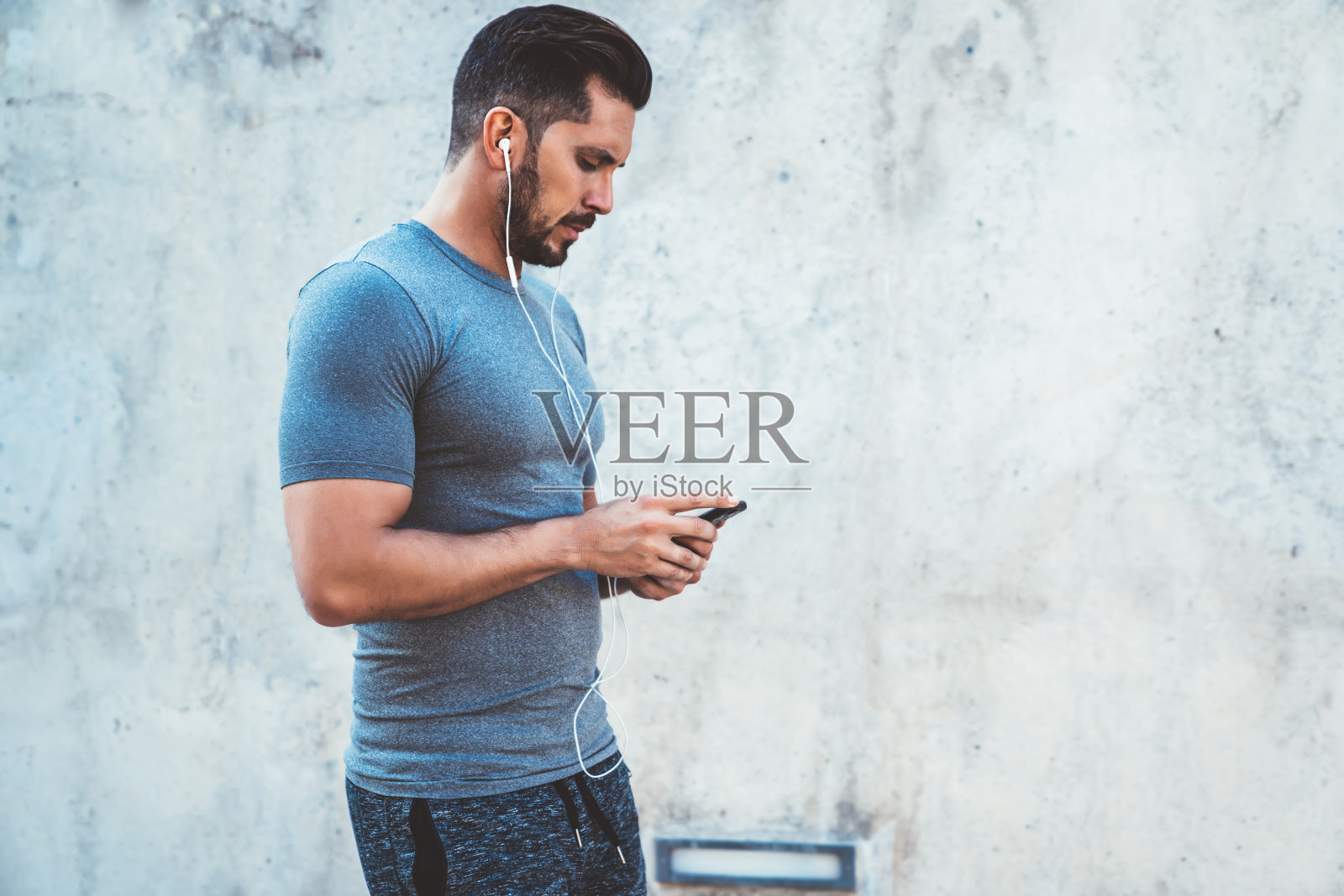 严肃的千禧男博主戴着耳机查看智能手机上的健身音乐下载通知，年轻的20多岁运动员使用应用程序记录活动结果和燃烧脂肪照片摄影图片