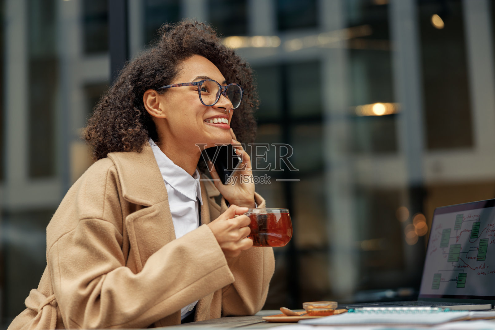 微笑的非洲裔美国女商人打电话，而工作在线坐在咖啡馆露台照片摄影图片