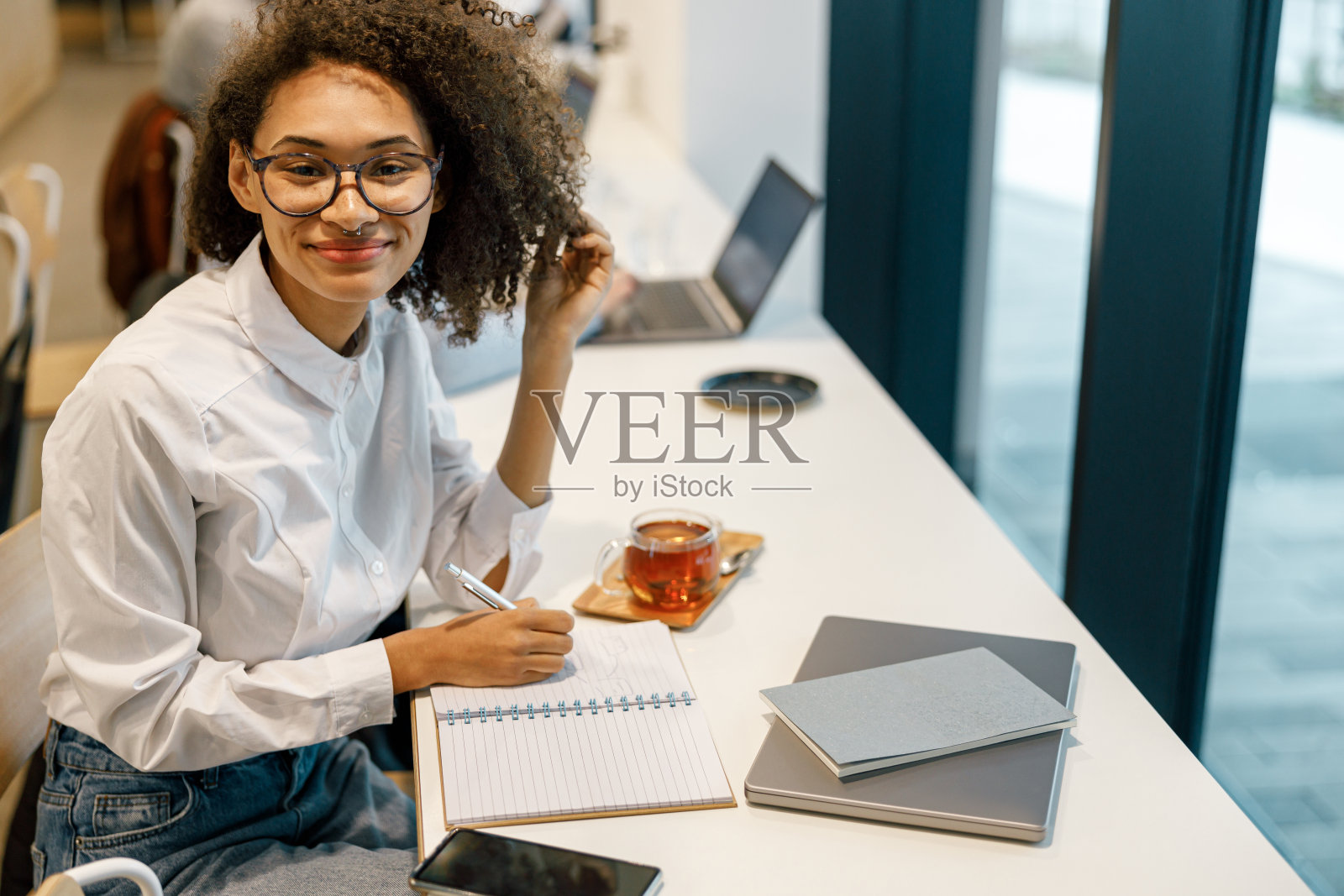 微笑的女人自由职业者工作笔记本电脑，并在舒适的咖啡馆坐在窗户附近做笔记照片摄影图片