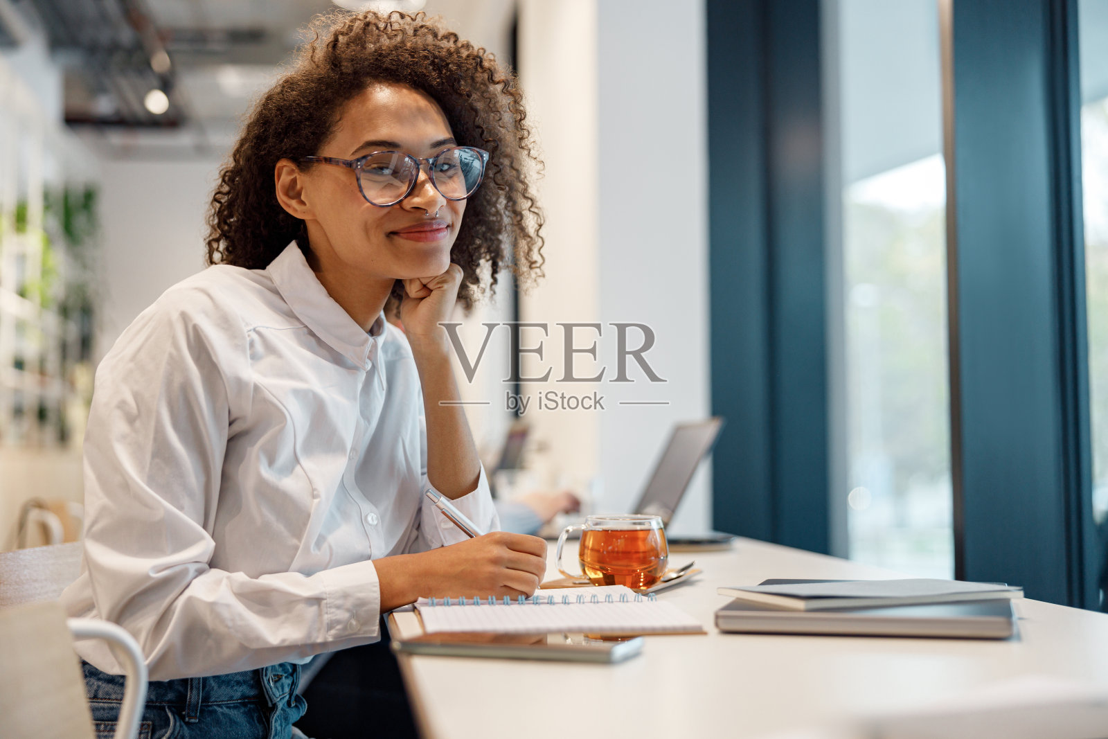 微笑的女商人工作笔记本电脑，并在舒适的咖啡馆坐在窗户附近做笔记照片摄影图片