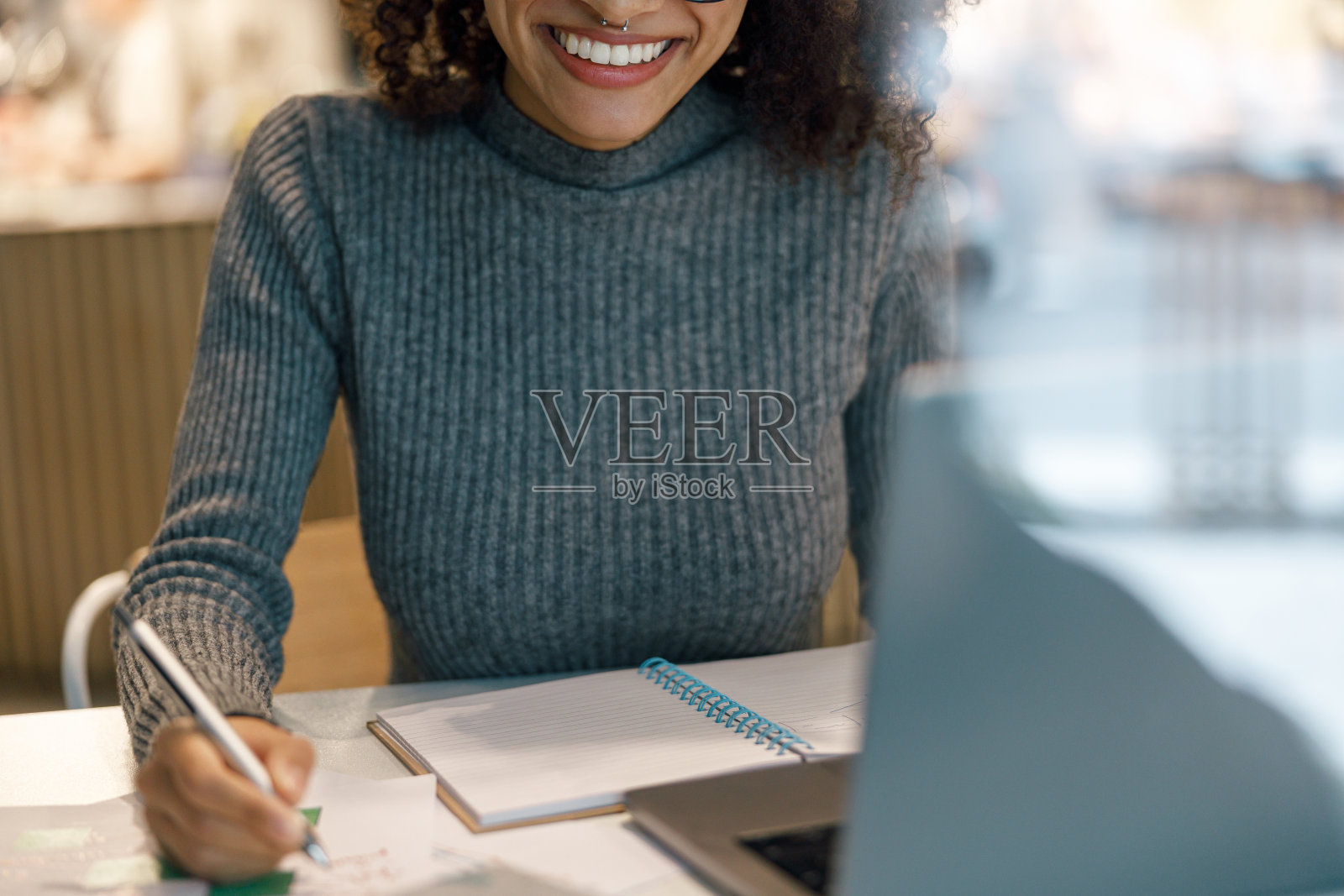 微笑的女人自由职业者工作笔记本电脑，并在舒适的咖啡馆坐在窗户附近做笔记照片摄影图片