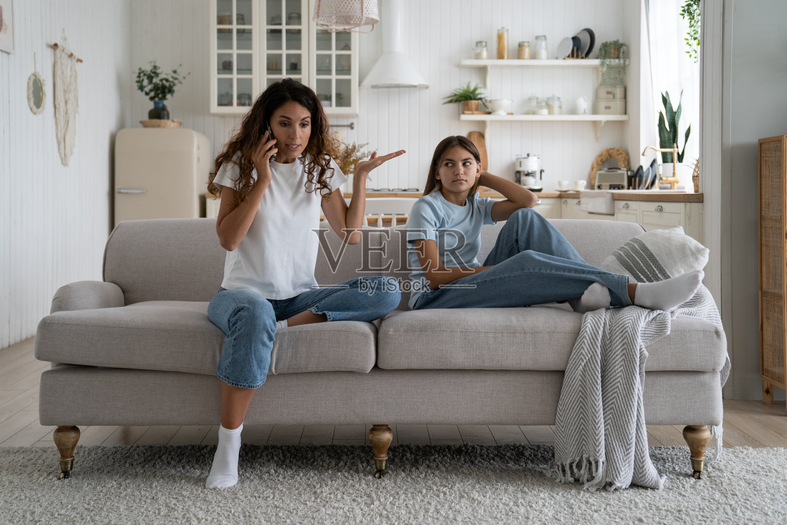 目瞪口呆的白人女子接听电话坐在客厅的沙发上，旁边是一个十几岁的女孩照片摄影图片