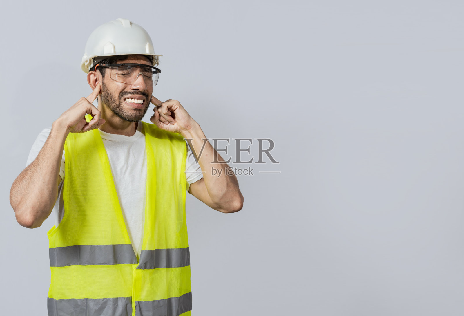 隔离耳朵疼痛的工程师，隔离耳朵疼痛的年轻工程师，隔离耳朵疼痛的建筑工人，工程师捂耳朵疼痛表情的概念。照片摄影图片