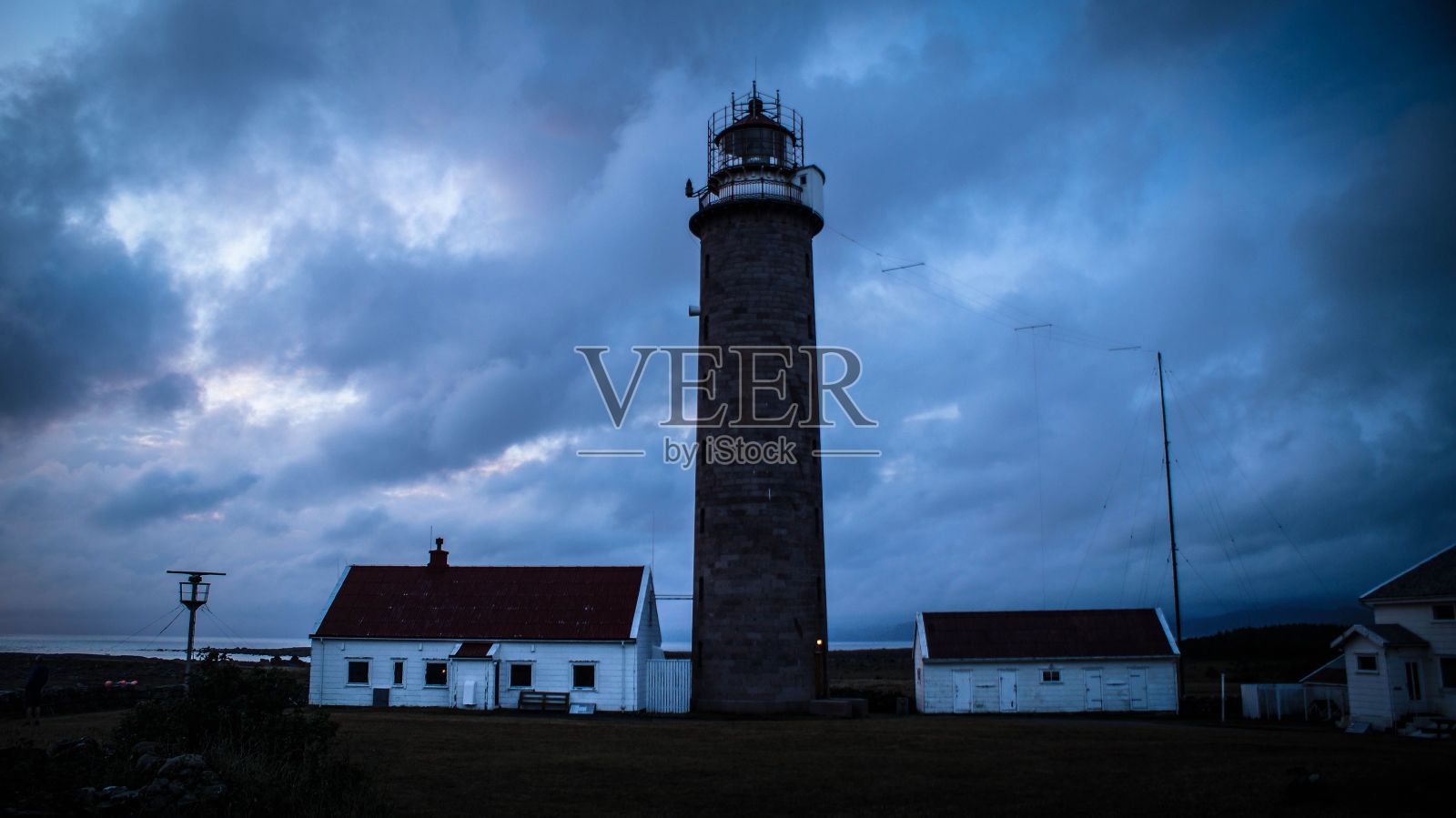 巨大的灯塔和白色的建筑孤立在阴郁的天空下的岸边照片摄影图片