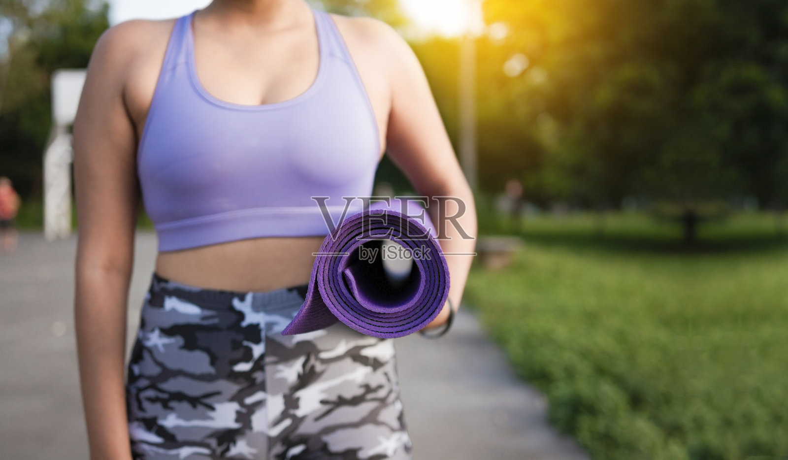 一个不认识的女人在公园里拿着垫子。女运动员锻炼后的手抬着垫子。健身女概念携带瑜伽垫与复制空间照片摄影图片