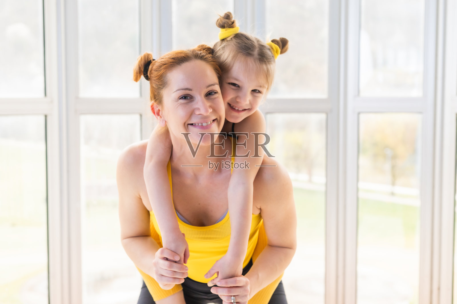 年轻健康的妈妈让她的女儿骑在背上。微笑着看着镜头照片摄影图片