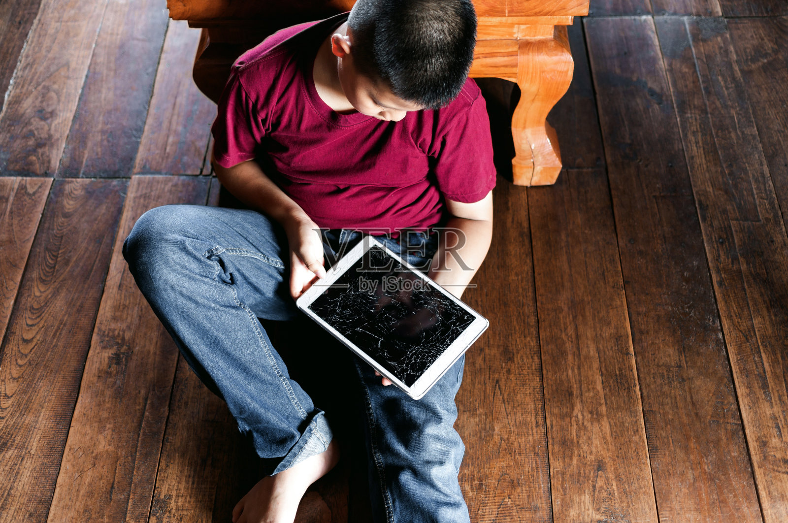 一个小亚洲男孩的肖像，孩子悲伤的脸，不开心的孩子坐着拿着坏了的平板电脑，情绪悲伤和悲伤的脸，抑郁的孩子概念照片摄影图片