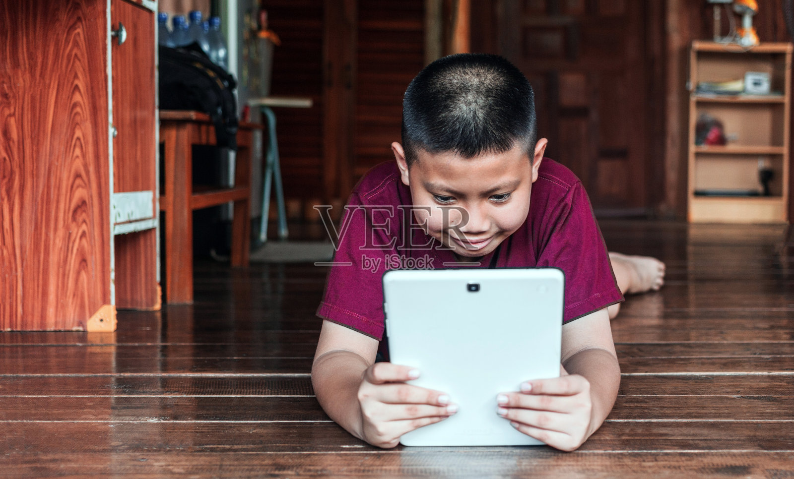 微笑的亚洲小男孩坐在家里的木地板上玩平板电脑。孩子在他使用智能设备与他的朋友在网上视频通话照片摄影图片