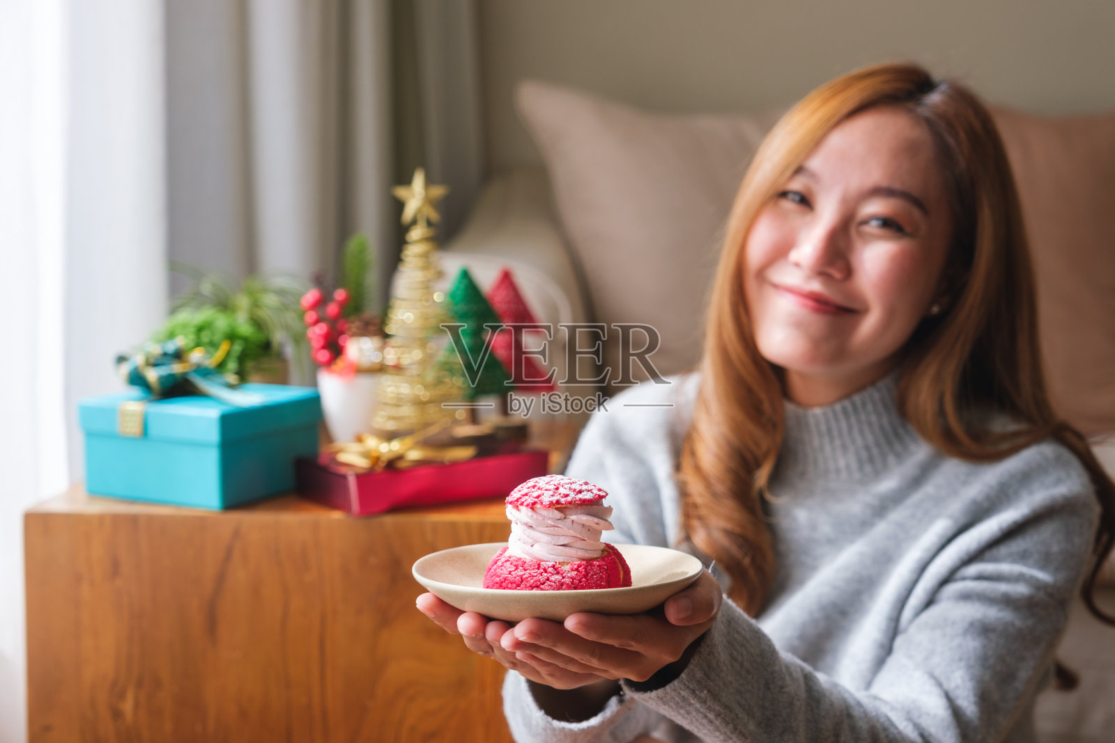 肖像图像的年轻女子在毛衣拿着泡芙蛋糕与圣诞节的节日装饰在家里照片摄影图片