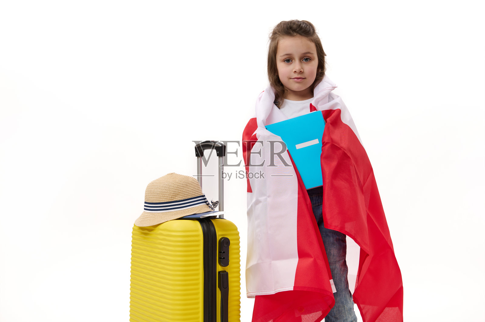 快乐的一年级学生，小女孩裹着加拿大国旗，拿着一本宣传册，在白色背景上摆出手提箱的姿势。照片摄影图片