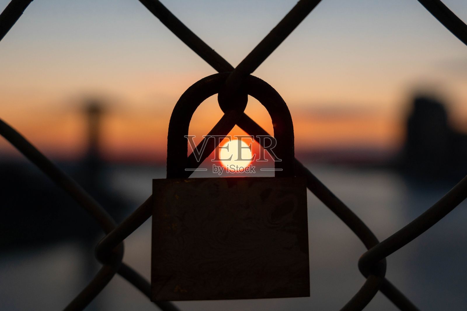 近距离剪影的便携式锁在围栏与日落可见的背景照片摄影图片