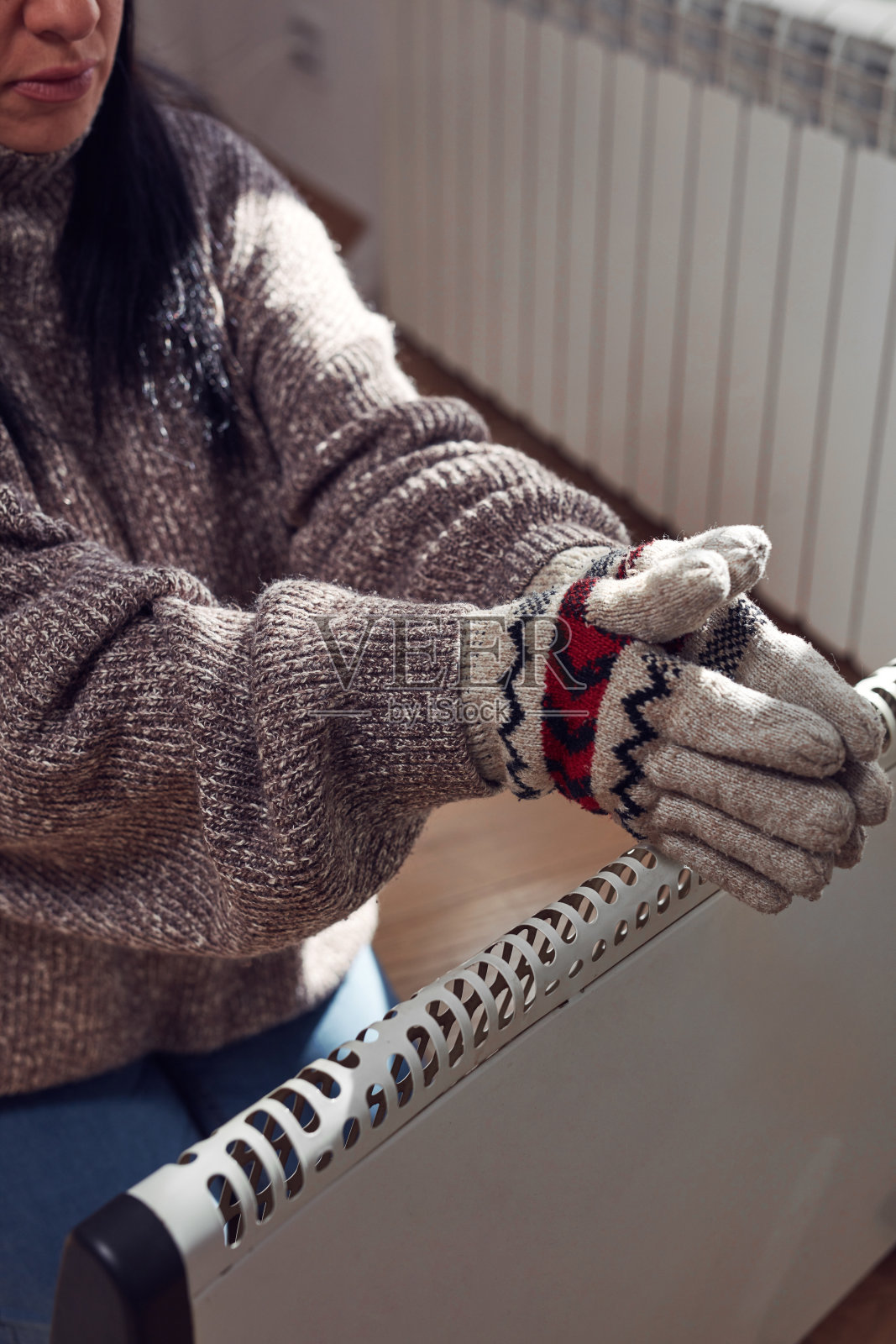 在寒冷的冬天，穿着夹克、毛衣和手套的妇女在室内，能源和天然气危机，寒冷的房间，供暖问题。照片摄影图片