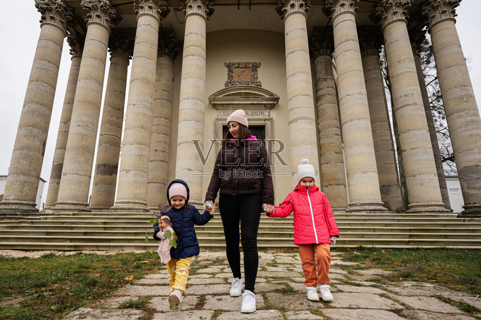 在乌克兰利沃夫州的皮得尔西，母亲牵着女儿们的手，站在巴洛克式的罗马天主教堂前。照片摄影图片