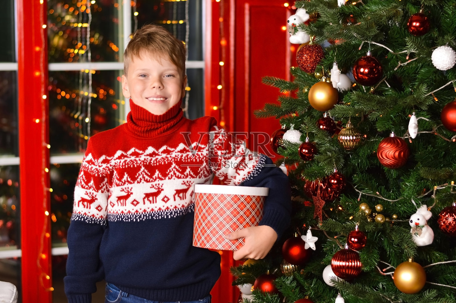 一个快乐的白人男孩在他的手中拿着圣诞礼物的肖像，对着灯光的背景。等待奇迹，童年。照片摄影图片