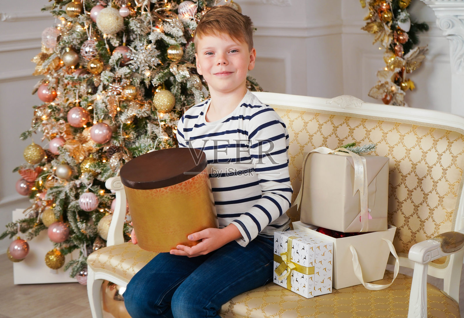 一个快乐的白人男孩在他的手中拿着圣诞礼物的肖像，对着灯光的背景。等待奇迹，童年。照片摄影图片