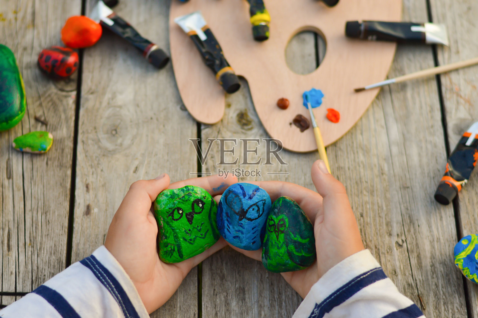 夏季室外车间。一个学生男孩手里拿着一块画好的扁平石头。自己动手吧。照片摄影图片