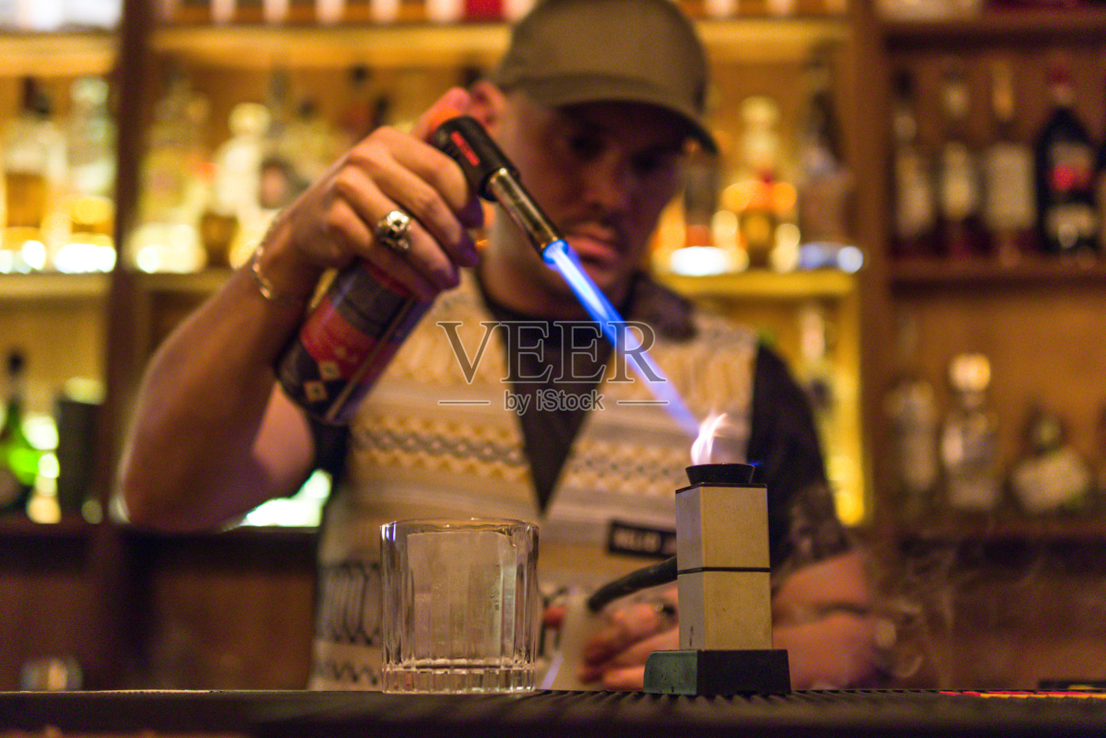 镜头聚焦在一个酒吧后面的酒保用喷灯点燃的香草烟装置上照片摄影图片