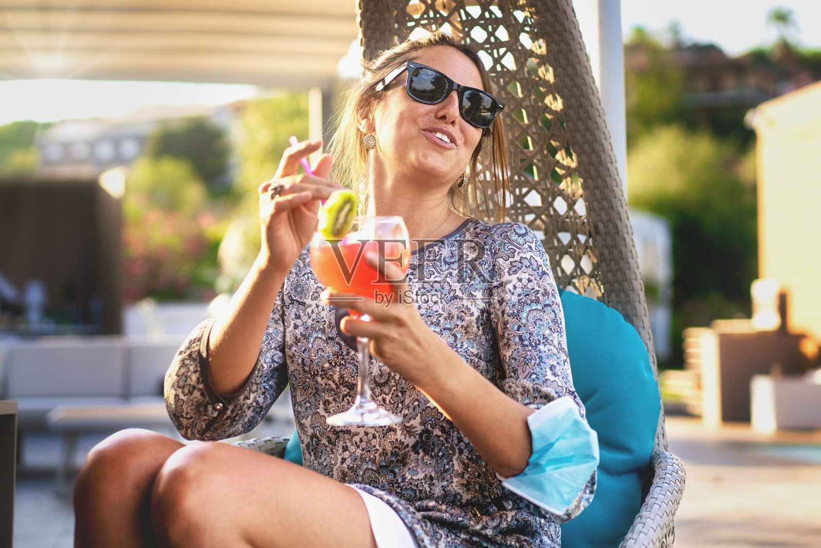 快乐的女人在度假派对上坐在花园摇椅上和她的朋友聊天，在一个温暖的夏天下午喝着多汁的健康鸡尾酒-健康的饮酒和人们的生活方式的概念照片摄影图片