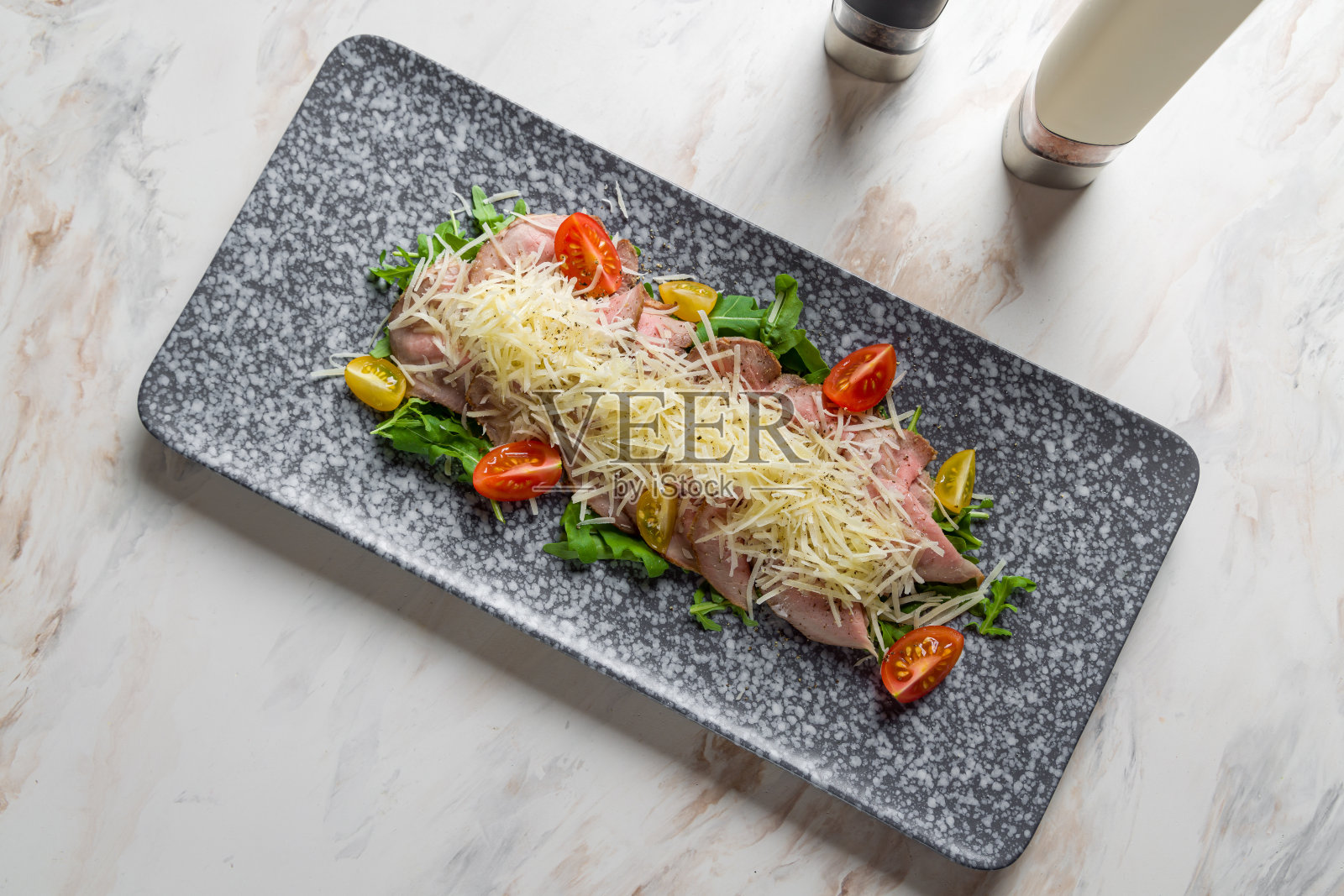 切片烤牛肉配芝麻菜，帕尔马干酪和西红柿放在大理石桌面上照片摄影图片