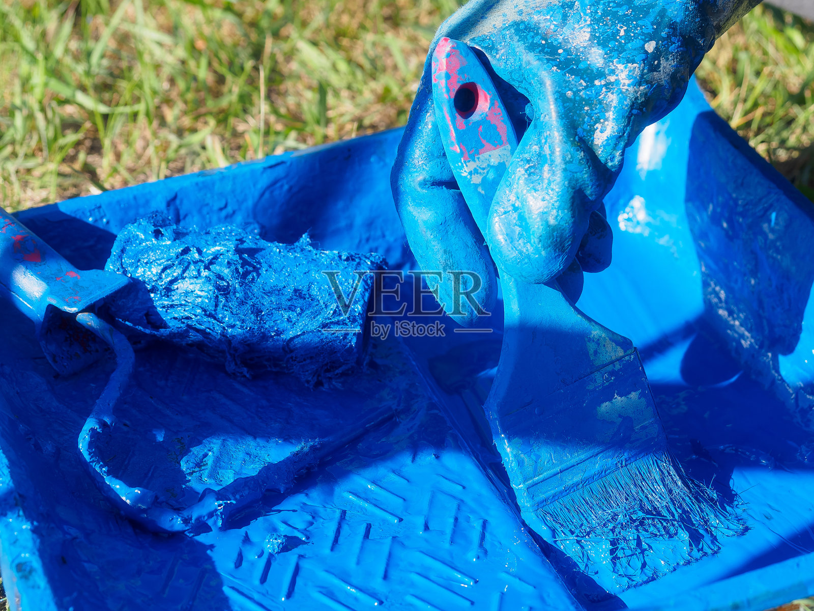 染色的托盘和油漆刷在蓝色油漆。工业油漆工戴着染色手套的手将油漆刷放在漆盘上。背景的特写镜头。照片摄影图片