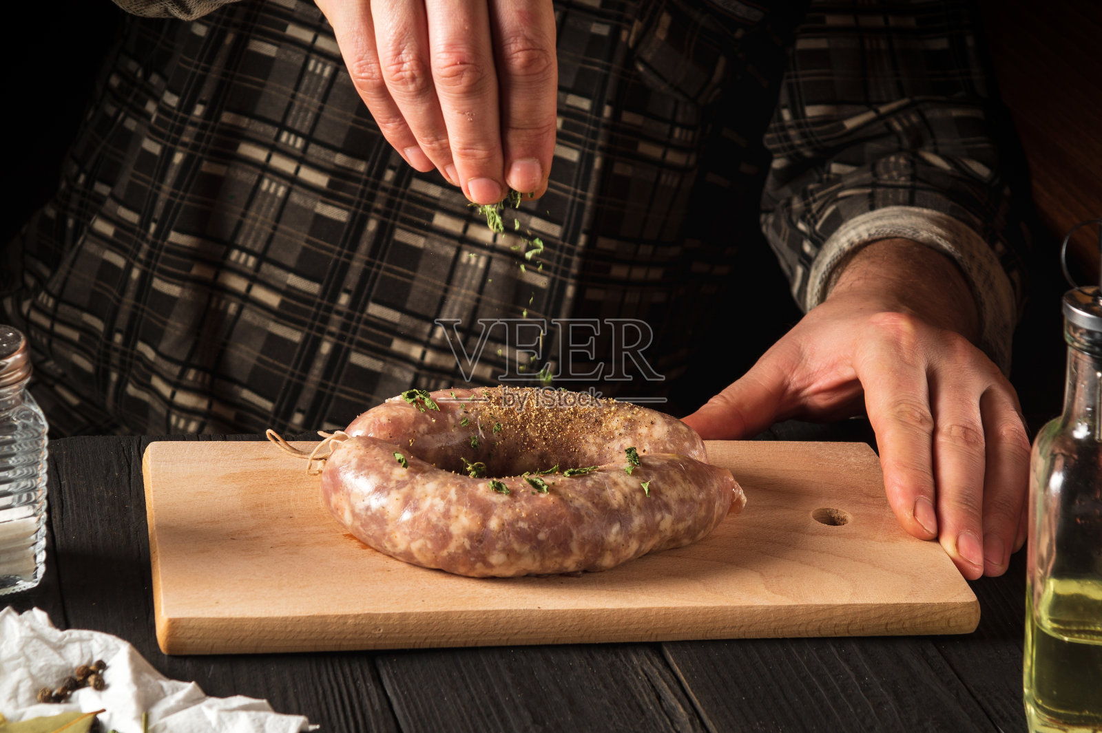 主厨给放在砧板上的自制香肠加香料。厨师的手合上了。餐厅或咖啡馆厨房的工作环境照片摄影图片