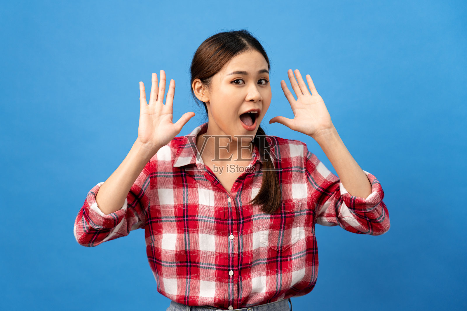 年轻的亚洲女子穿着格子红色衬衫与辫子发型和兴奋的脸，而使用手听照片摄影图片