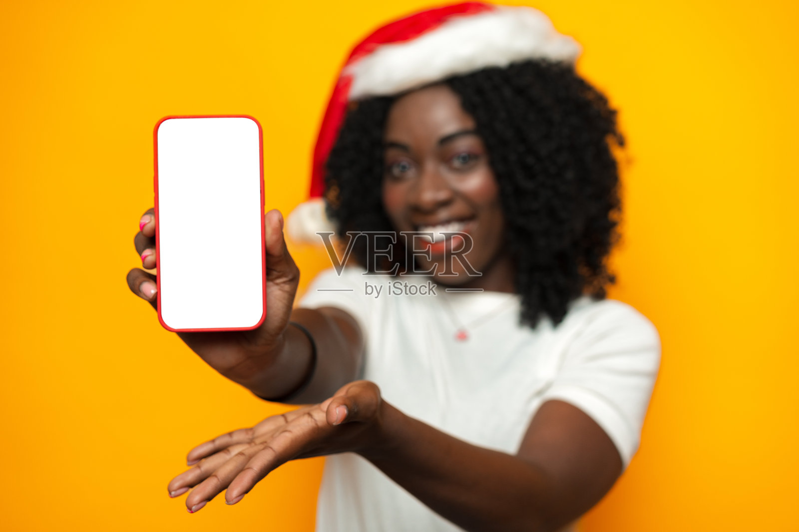 美丽的非洲女人戴着圣诞老人帽子，手机上有空白的copyspace屏幕照片摄影图片