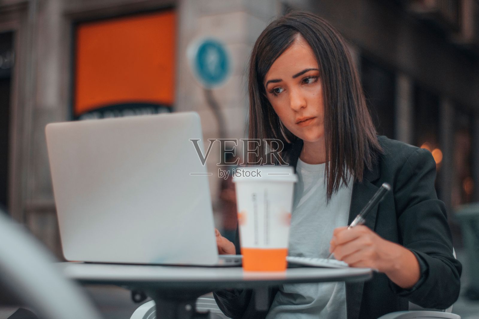 年轻的白人女商人一边看着笔记本电脑一边写东西照片摄影图片