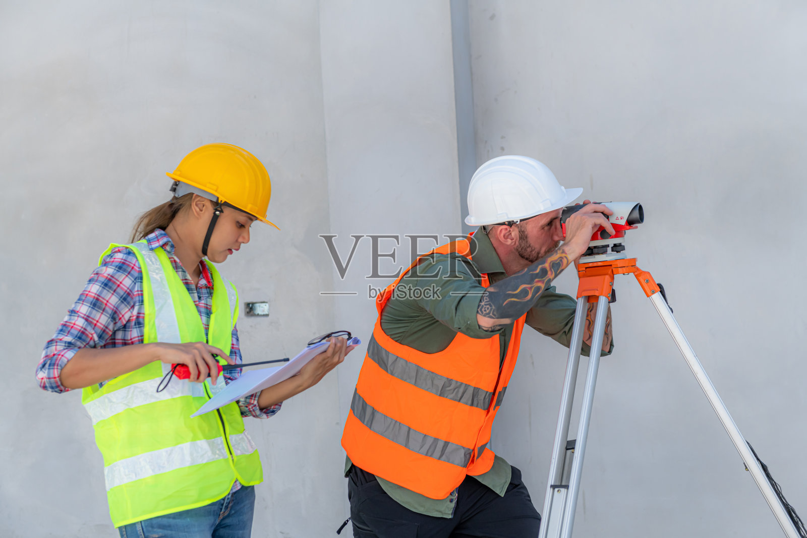 建筑工人在施工现场使用经纬仪测量光学仪器测量水平面和垂直面的角度。工程师和建筑师在测量师旁边使用平板电脑。照片摄影图片