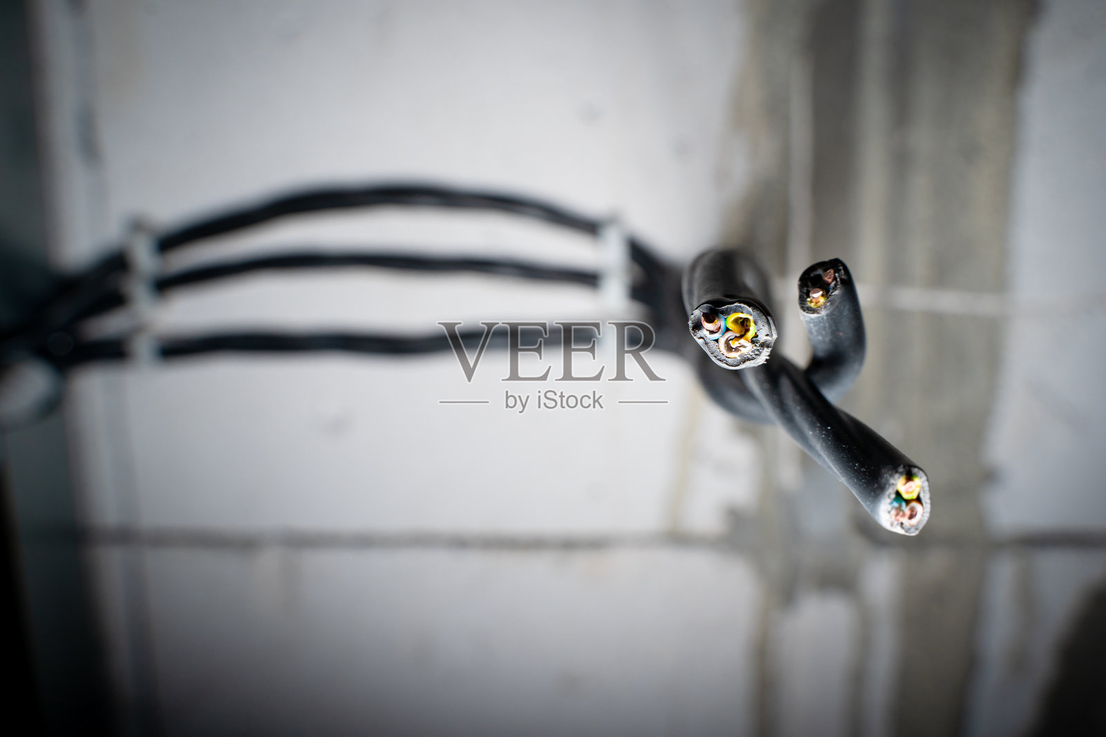 电力三芯铜电缆特写。私人住宅墙上的电线。固定电力电缆敷设在裸露的墙壁上，无需维修。在模糊的背景上切断电线照片摄影图片